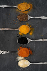 Various spices on tablespoons on a slate plate