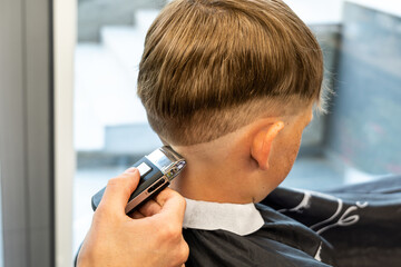 Barber cuts red-haired client occiput with adjustable trimmer in barbershop closeup. Professional...