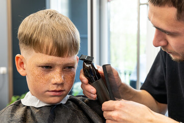 Picture in a barbershop studio with a small boy with very beautiful blue eyes and a very attractive...
