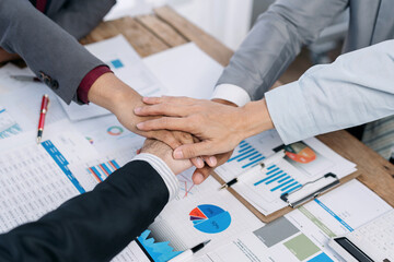 A group of people are shaking hands on a table with a lot of papers and graphs