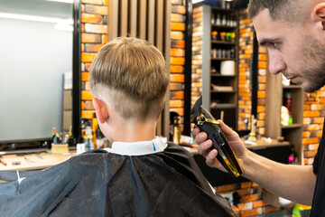 A blond and freckled child is seated on a chair in the barbershop and is trimmed by a true professional in the field.