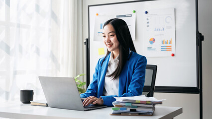 A woman is sitting at a desk with a laptop and a stack of papers