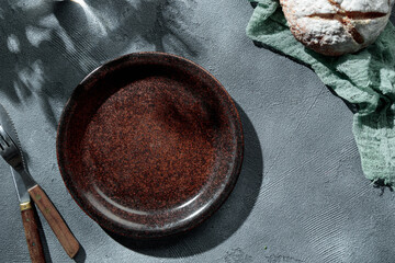 Brown rustic empty plate, cutlery and napkin on stone table top view, sunny day, shadows, summer....