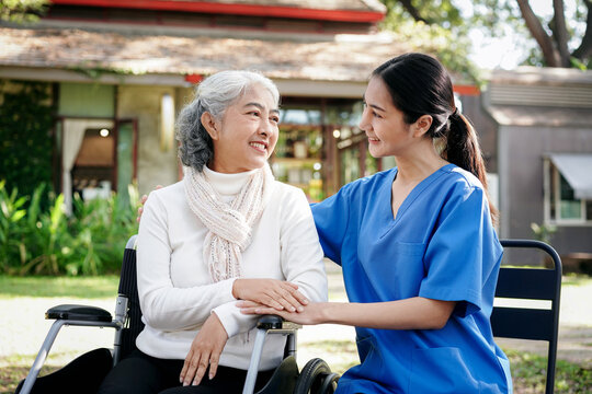 A woman in a blue uniform is sitting next to an elderly woman in a wheelchair