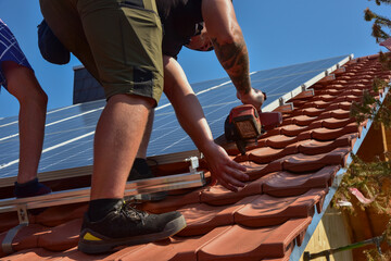 Dachdecker beim Aufbau einer Photovoltaikanlage auf einem neu gedeckten Ziegeldach: K&uuml;rzen der Schienen mit der Trennscheibe an der Position der Endklemme
