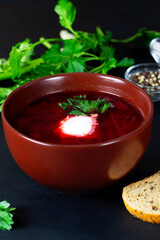 delicious red borscht with sour cream, green parsley on the black background. red beet soup in the...