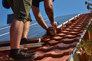 Dachdecker beim Aufbau einer Photovoltaikanlage auf einem neu gedeckten Ziegeldach: Kürzen der...
