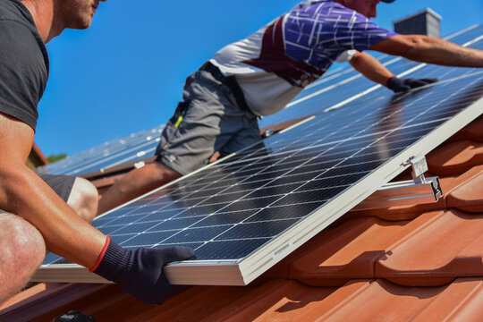 Dachdecker beim Aufbau einer Photovoltaikanlage auf einem neu gedeckten Ziegeldach: Verschraubung der Solarmodule an den Endklemmen des Schienensystems am Dachrand