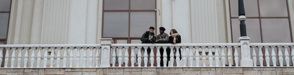 Three friends enjoying casual conversation on balcony of historical building.