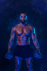 Sporty fit man athlete with dumbbells make fitness exercises on neon background. Download cover for music collection for fitness classes. Sports recreation.