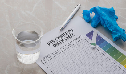A daily water pH check report on the table. Glove, water test strip, pen  and beker with water...