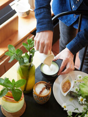 Woman pouring milk into cup of cappuccino in coffee shop