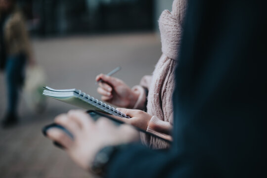 Close-up of young entrepreneurs analyzing data and networking with digital tablet and notepad in a city environment, focused on business expansion.