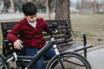 Obraz premium Active young kid resting on park bench with his bicycle, enjoying a day outdoors.