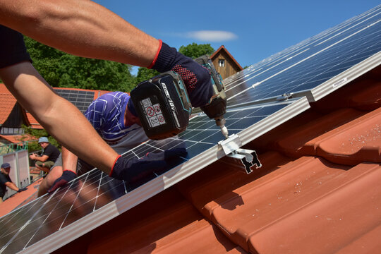 Dachdecker beim Aufbau einer Photovoltaikanlage auf einem neu gedeckten Ziegeldach: Verschraubung der Solarmodule an den Endklemmen des Schienensystems am Dachrand