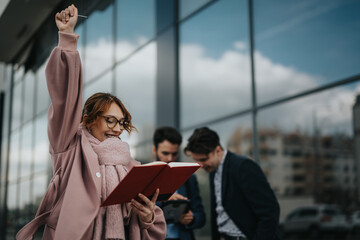 A group of business colleagues showing excitement and success with a raised hand outside their...