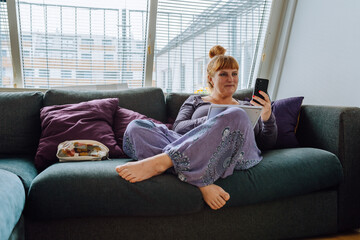 portrait middle-aged woman in home clothes sitting on sofa using a phone