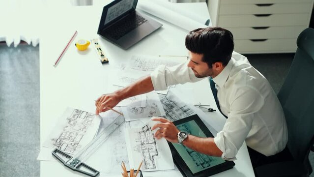 Architect engineer using laptop planning house design at office while sitting at meeting table with blueprint and equipment scatter around.Skilled civil engineer working at blueprint. Alimentation.