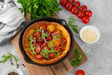 Savory cheese Dutch baby pancake. Dutch Baby pancake with mix tomatoes, parsley and arugula in cast iron pan on a concrete background. Delicious healthy breakfast.