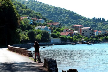 A girl in shorts stands next to a bicycle on a pier near the Bay of Kotor in the Adriatic Sea
