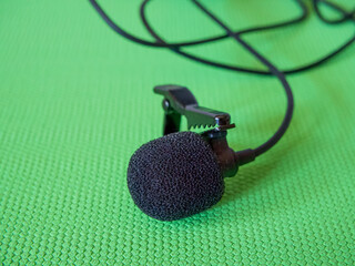 Lavalier Microphone Detail. A black lavalier microphone with foam windscreen and clip on a green...