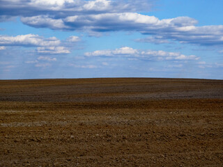 Horizon view of an open field with scattered clouds above.
