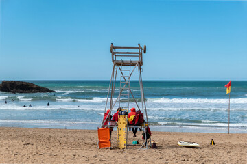 Torre de vigilância com alguns socorristas a garantirem a segurança dos banhistas e surfistas que desfrutam das ondas - obrazy, fototapety, plakaty