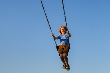 Kid swinging high. Adorable blonde child having fun on a swing on playground. Happy kid swinging on playground area. Summer playground. Child swinging high.
