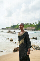 Flamboyant gay black male in luxury gown poses on scenic ocean beach. Trans sexual ethnic fashion...