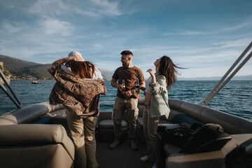Friends laugh and relax, drinking beers on a boat trip, surrounded by the expansive sea under a...