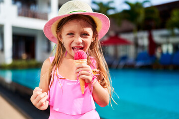 Little girl in pink swimsuit enjoys strawberry ice cream by poolside. Happy child relaxing after swim, savoring sweet treat on sunny day. Summer vacation, outdoor leisure for kids, refreshment.