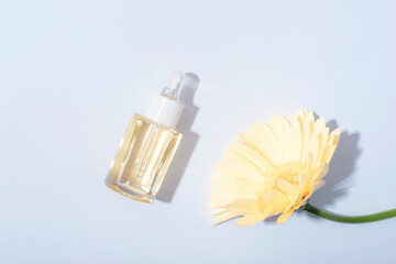 Cosmetic serum bottle, yellow gerbera flowers on a white background in sunlight. Top view, flat lay