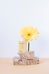 Cosmetic serum bottle on stone podium with yellow gerbera flower on a white background. Front view