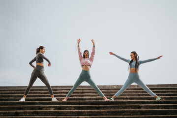 Active women practicing yoga together on outdoor steps, promoting health and wellness.