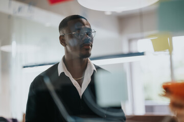 Focused young entrepreneur brainstorming with sticky notes on a glass wall, sharing ideas and discussing statistics in a contemporary office setup.