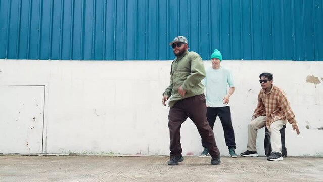 Skilled hipster doing cart wheel while multicultural friends encourage him. Hip-hop dancer moving foot step to music surrounded by group of hipster at wall near street. Outdoor sport 2024. hiphop.