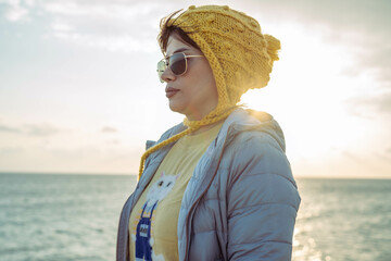 A woman with autumn style wearing a yellow hat and a blue jacket by the sea above the coral reef.