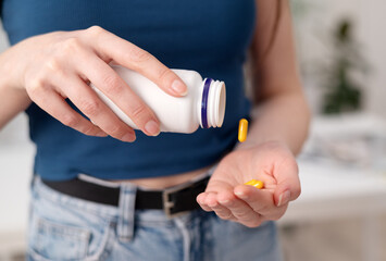 Young woman holds yellow pills in a hand, female takes supplements and vitamins from a bottle, close-up view.
