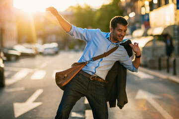 Happy young businessman walking on city street at sunset