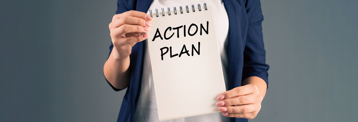A woman holding a notepad with "action plan" written on it, on a gray background, stock photo