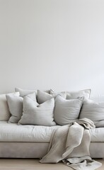 A light gray sofa with soft cushions, beige blanket and pillows against a white wall