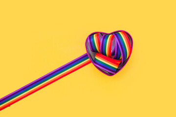 Lgbt rainbow ribbon in a heart shape on bright color background. Gay pride month, coming out day, close up, tolerance concept. Flat lay. top view, place for text or logo - obrazy, fototapety, plakaty
