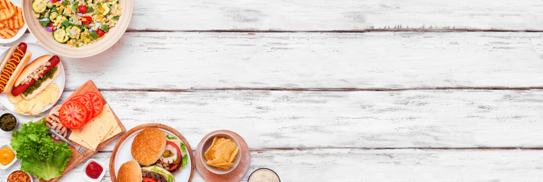 Summer BBQ or picnic corner border with hamburgers, hotdogs, salad and snacks. Above view over a white wood banner background. Copy space.