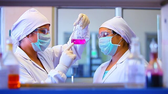 two chemist scientists and mixing chemicals. chemist experimenting. science experiment in a beaker flask titration with colorful pink chemicals liquid in laboratory with medical lab equipment.	
