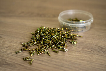 Metal screws in a plastic box are on the table.The mounting screws are gold in color.