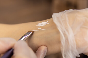 Woman applies white eyebrow marking paste on hand. Swatch of eyebrow paste. Soft focus