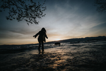 A girl stretches her arms out in happiness by a lakeside, with the tranquility of a spring sunset...