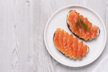 Rye sandwich with salmon and cream cheese on white wooden table, with copy space for text