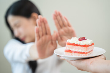 Dieting young asian woman or girl use hand push out, dent sweet cake and control temptation for dessert.