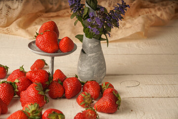 Strawberries and a vase with flowers on a wooden table. A wonderful summer picture of flowers and fresh berries
